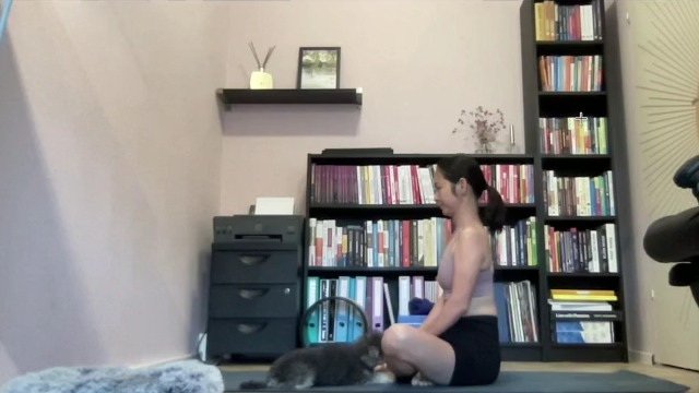 A student sits on a yoga mat, seen from the side, during the posture observation part of an alignment lesson.