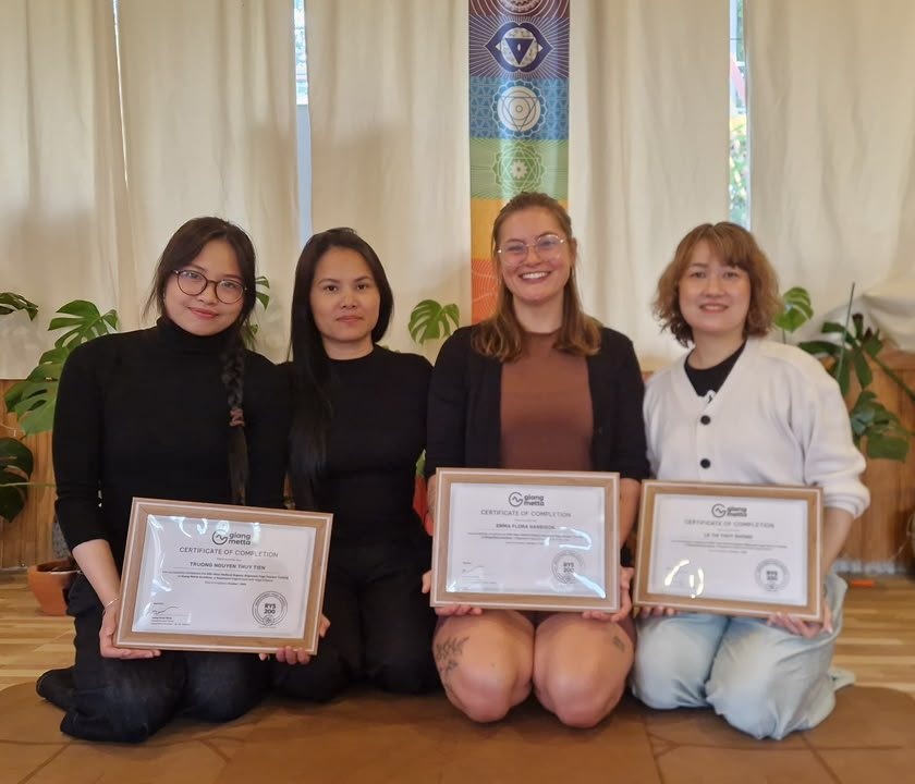 Four graduates of Giang Metta's 200-hour yoga teacher training kneeling with their certificates in Da Lat