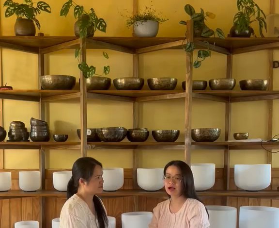 Kệ gỗ trên tường vàng: hàng trên là chuông xoay Tây Tạng bằng kim loại, hàng dưới là chuông xoay pha lê trắng; Thanh và người hỏi ngồi phía trước.